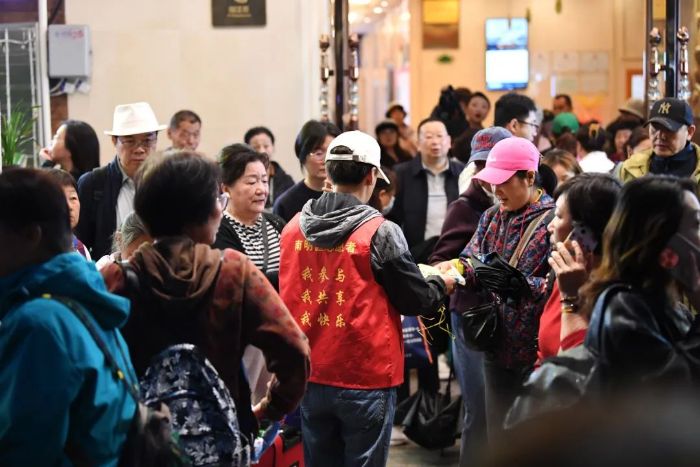 4月24日,在贵阳市南明区花果园,社区志愿者正在为出行的游客发放一次性雨衣。 图片