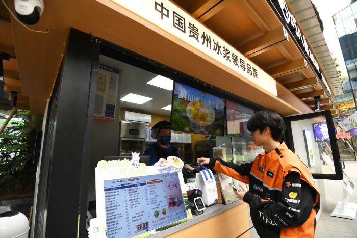 6月10日,在贵阳市南明区花果园购物中心,取货端“步兵”派送员正在一冰浆冰粉店取外卖。 图片